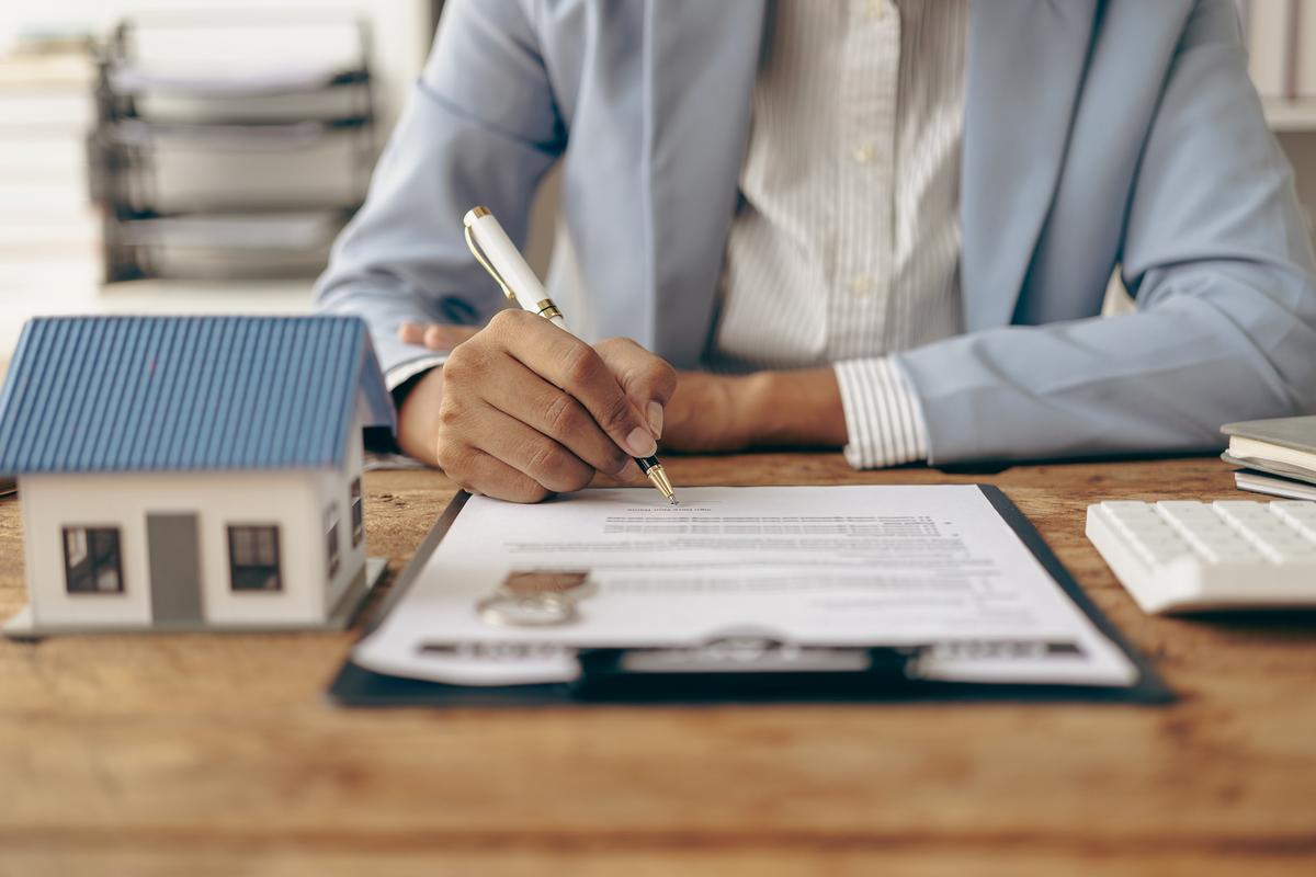 Man signing a document with model house beside him